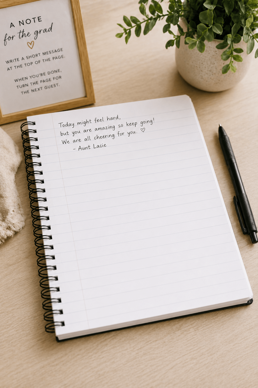 Open notebook with a short handwritten encouragement at the top of the page and the rest left blank for notes, styled with a pen and simple graduation guest book sign.