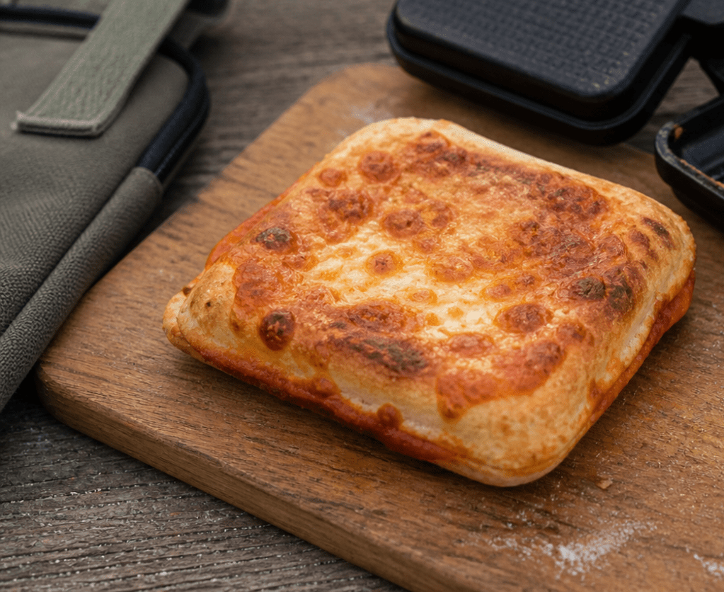 Cooked campfire pizza pocket on a wooden board next to an open pie iron